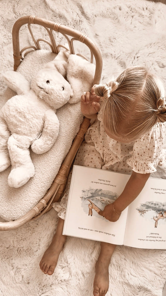 Meisje leest rustig een boek in bed naast de Konijn-verzwaringsknuffel tijdens de avondroutine