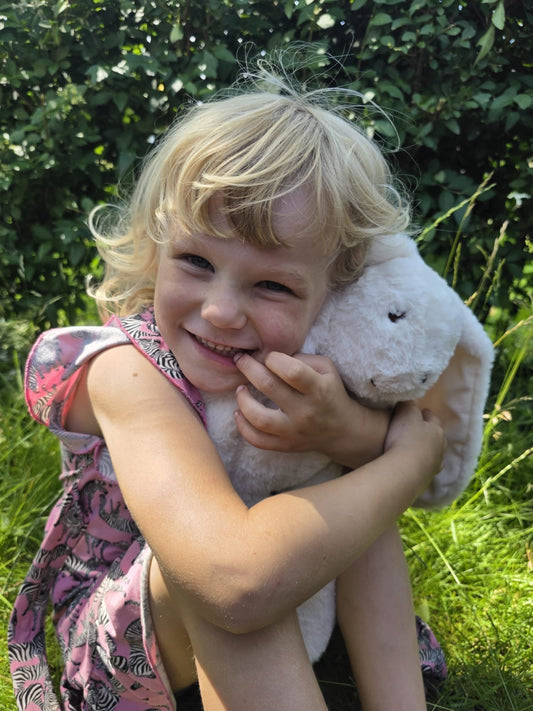 Lachend meisje knuffelt de Konijn-verzwaringsknuffel buiten in de tuin