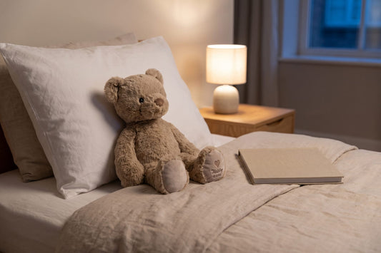 Verzwaringsknuffel Beer tegen een kussen op bed, met een nachtlampje aan